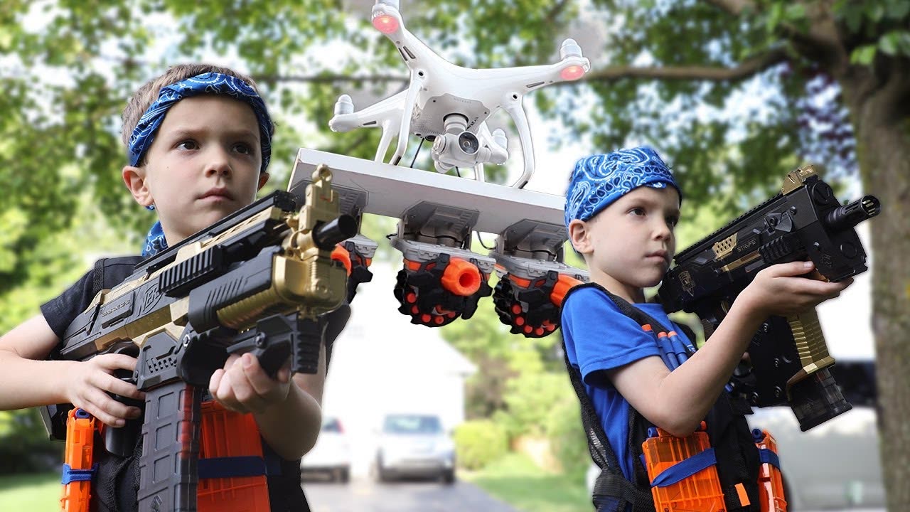 Two boys with Nerf blasters under a drone carrying blasters